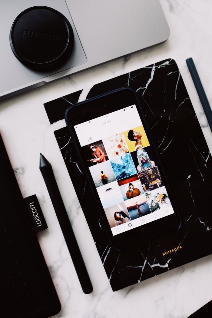 Black organizer with mobile phone app demonstrating creative images on screen and cup located on laptop touch pad near marker put on marble table