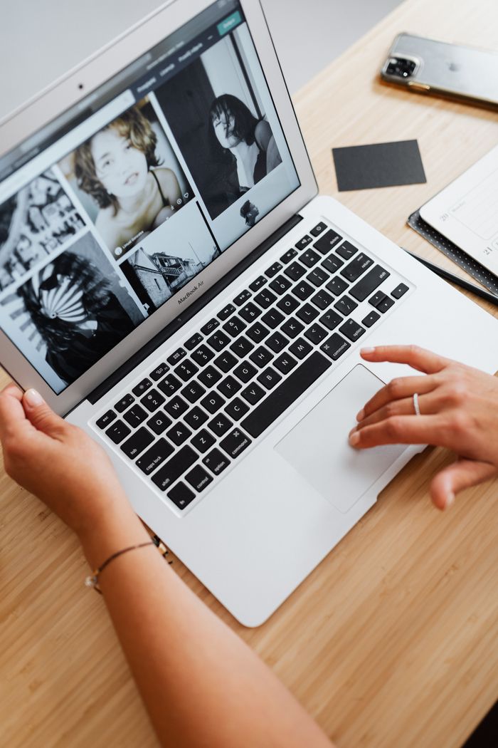 Hands on laptop browsing photos, wooden desk setup. Perfect for depicting digital workspace themes.