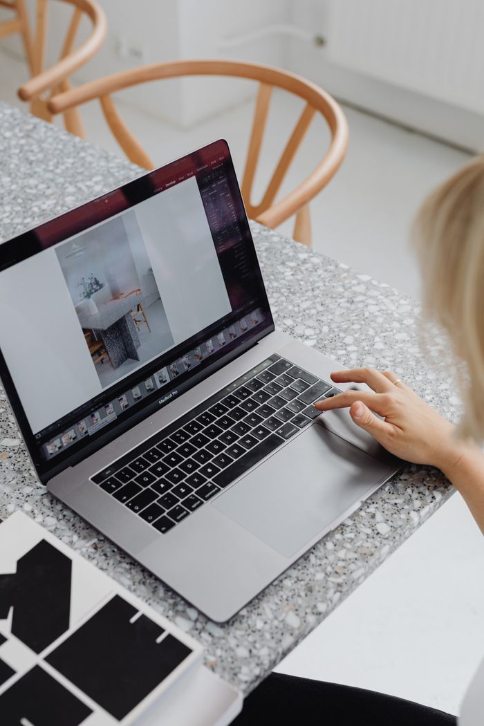 Overhead view of a woman using a laptop on a stylish marble table, displaying a design layout.