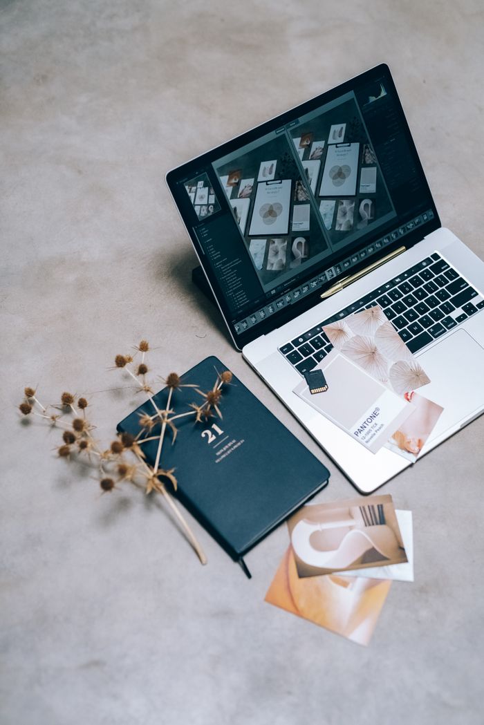 A high-angle shot of a creative workspace featuring a laptop, planner, and dried flowers on a flat surface.
